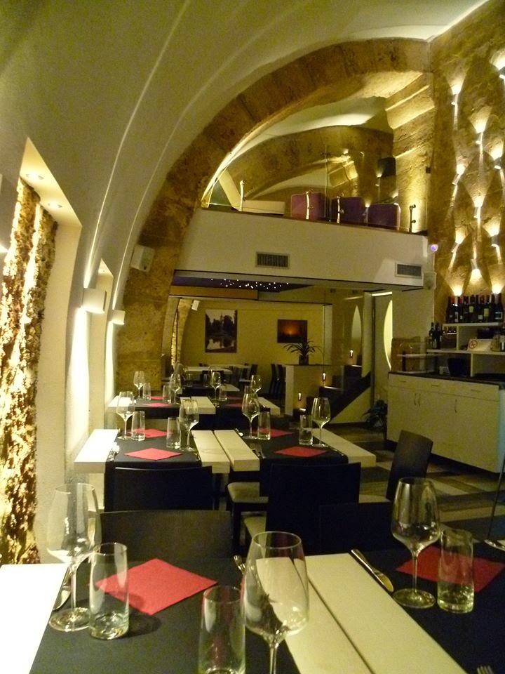 La sala di Carizzi d'amuri: volte bianche a botte sopra archi in pietra illuminati dal basso, tavoli con tovaglia bianca e tovagliolo rosso piegato.